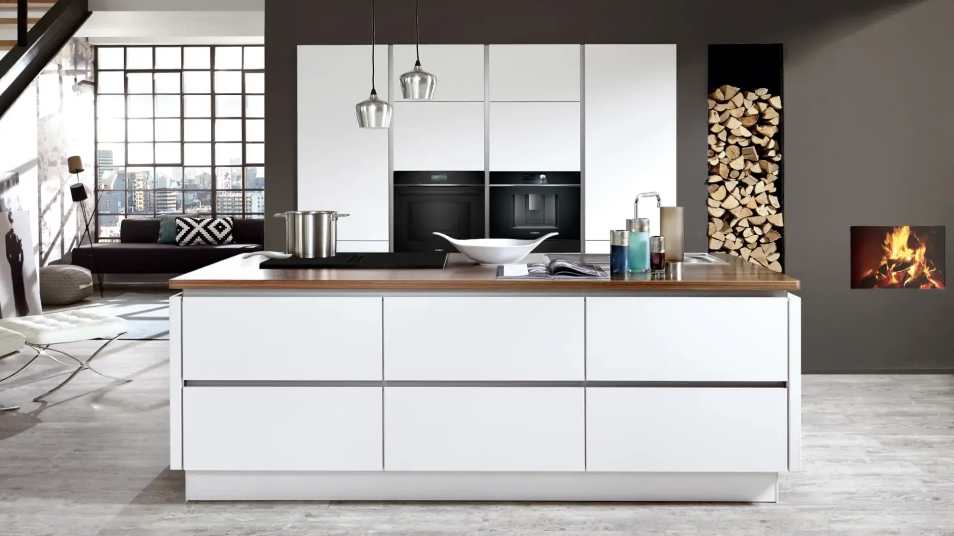 Moderne weiße Küche mit Kochinsel, eingebauten schwarzen Geräten, Holzofen und Holzstapel.