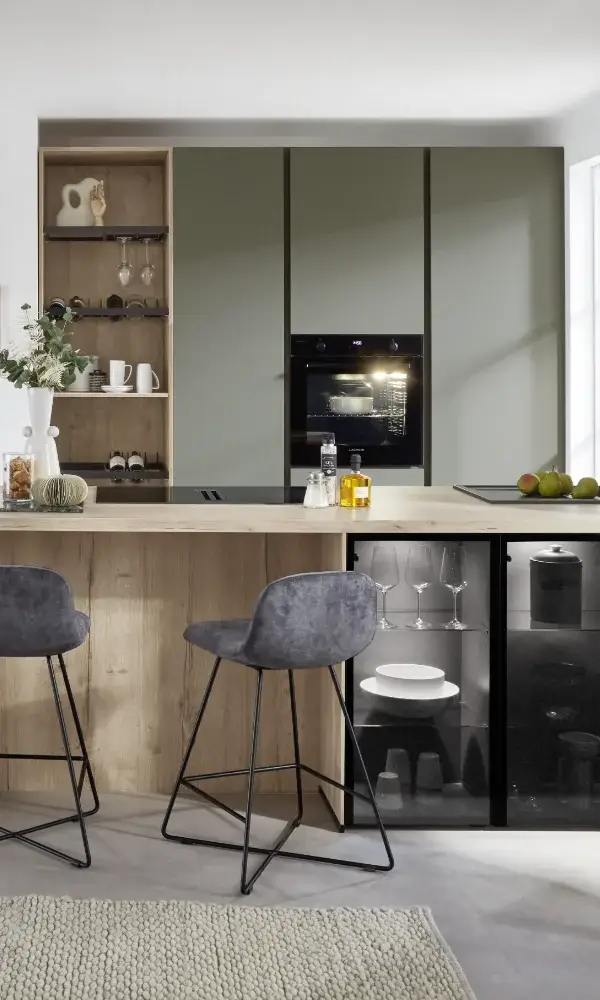Moderne Küche mit grauen Schränken, eingebautem Ofen, Barhockern und offenem Regal mit Gläsern.