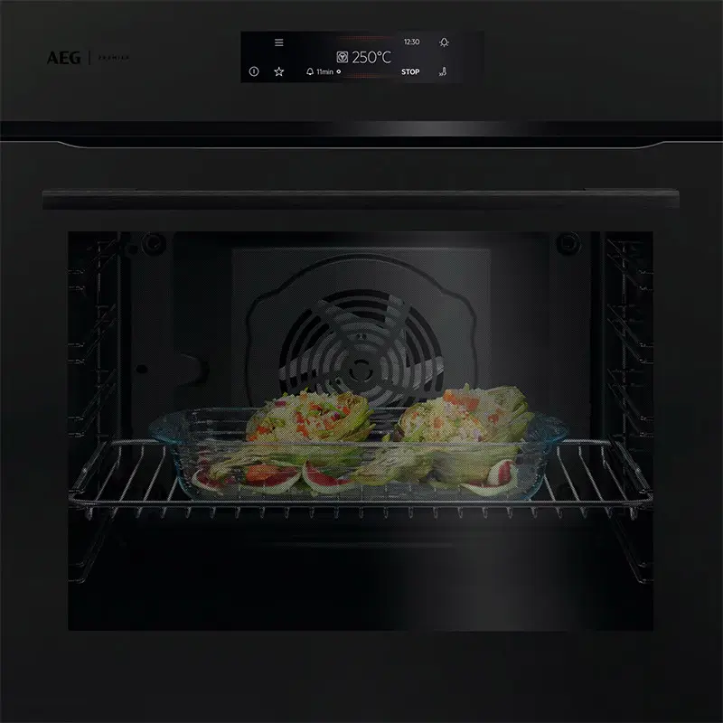 Ein schwarzer Einbaubackofen von AEG mit einer digitalen Anzeige, die 250 °C anzeigt, und einem Glasbehälter mit gefülltem Gemüse im Inneren.